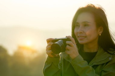 Bir kadın kamp gezisi sırasında dağ zirvesinde gün batımının fotoğraflarını çekiyor.