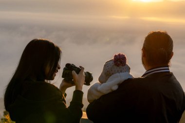 Bir aile sabahın erken saatlerinde bir dağın zirvesinde güneşin doğuşunun fotoğraflarını çekiyor..
