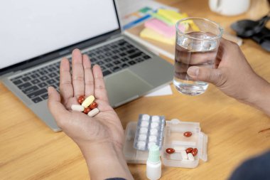 Uzun saatler masa başında çalıştıktan sonra ağrı kesici alan bir iş adamının arka görüntüsü.