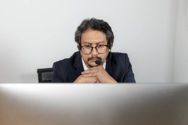 Sanal bir toplantıda, bilgisayar ekranına odaklanmış ciddi bir iş adamı.