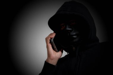 Başkalarını kandırmak için akıllı telefon kullanan maskeli bir adam, telefon dolandırıcılığı ve dolandırıcılık kavramı