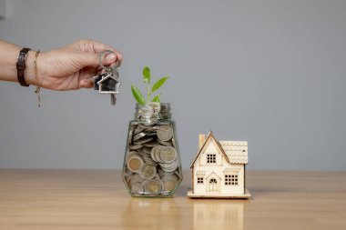 Ev için para biriktirmek, bir elin yakın plan çekimi kavanoza bozuk para koymak, finansal hedefleri ve sorumluluğu simgeliyor.