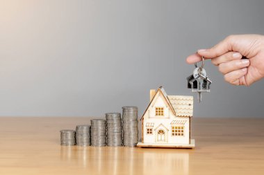 Küçük ev modelinin yanında el ele tutuşmanın anahtarı, yeni bir ev ya da mülk almayı sembolize ediyor.