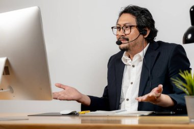 Mutlu ofis çalışanı kulaklık takıyor, modern çalışma yerinde sanal bir toplantının keyfini çıkarıyor..