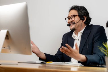 Mutlu ofis çalışanı kulaklık takıyor, modern çalışma yerinde sanal bir toplantının keyfini çıkarıyor..