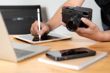 Yaratıcı çalışma alanında dijital tablet kullanarak fotoğraf rötuşlama üzerinde çalışan genç fotoğrafçının eli.