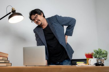 Uzun süre oturmaktan sırtı ağrıyan Asyalı erkek ofis çalışanı, işle ilgili sağlık sorunları gösteriyor.