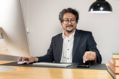 Neşeli genç bir erkek işçi masasında modern bir ofiste çalışıyor, iş memnuniyetini, verimliliği ve pozitif çalışma ortamını temsil ediyor..