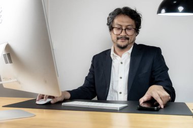 Modern ofis ortamında masasında çalışan neşeli bir erkek ofis çalışanı verimliliği ve iş memnuniyetini temsil ediyor..