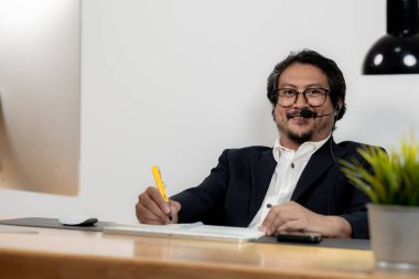 Genç bir erkek ofis çalışanı bir video konferansına katılmak için masada oturuyor..