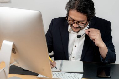 Genç bir erkek ofis çalışanı bir video konferansına katılmak için masada oturuyor..