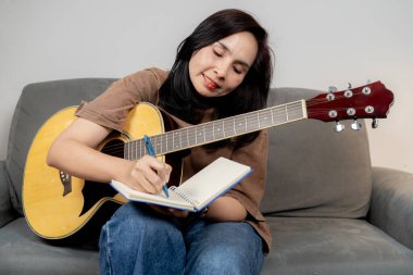 Evde akustik gitar çalarken koltukta oturup müziğin tadını çıkaran rahat bir kadın..