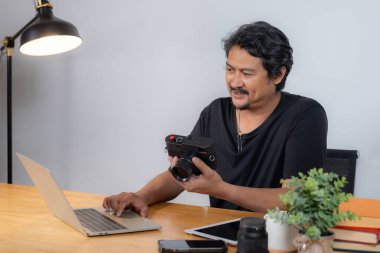 Evden çalışan genç bir erkek fotoğrafçı rahat bir çalışma alanında yaratıcı bir yazılımla bilgisayardaki fotoğrafları düzenliyor.