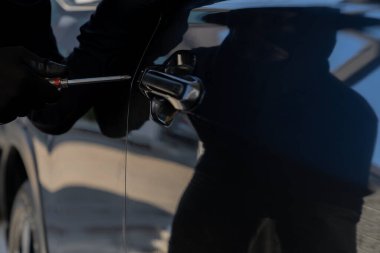 Siyah elbiseli bir suçlu gece park halindeki bir arabaya girmeye teşebbüs, araba hırsızlığı, güvenlik riski ve suç önleme kavramı.