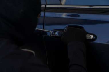 Siyah elbiseli bir suçlu gece park halindeki bir arabaya girmeye teşebbüs, araba hırsızlığı, güvenlik riski ve suç önleme kavramı.