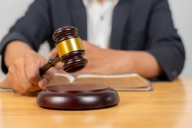 Arka planda bir yargıcın olduğu tokmağın yakın çekimi, hukuku, hukuki işlemleri, adaleti ve mahkeme otoritesini simgeliyor.