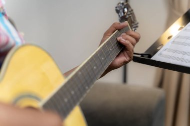 Akustik gitar panosundaki akorlara basan bir elin yakın plan görüntüsü, odak noktasındaki telleri ve parmakları vurguluyor.