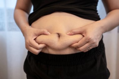 Genç bir kadının göbeğini sıkması, kilo kaybı, vücut bakımı, diyet ve sağlıklı yaşam tarzı farkındalığı..