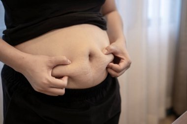 Genç bir kadının göbeğini sıkması, kilo kaybı, vücut bakımı, diyet ve sağlıklı yaşam tarzı farkındalığı..