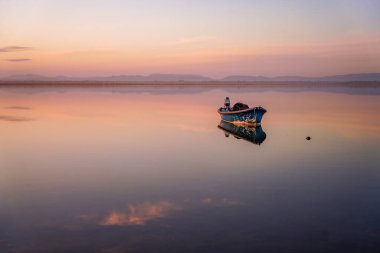 Gün doğumunda, ufukta sakin bir yüzeyle denizde bir teknenin dikey görüntüsü.