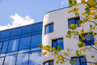 mavi gökyüzü arkaplanına karşı yeşil ve sarı yapraklı modern apartman