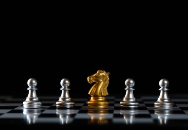 Altın şövalye satranç taşı, gümüş piyonlarla çevrili siyah arka plan tahtasının üzerinde duruyor. Yönetim, liderlik ve stratejik yaratıcılık kavramı. İş fikri stratejik planlama ve düşünme.