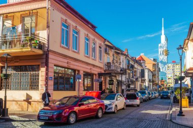 Canlı kırmızı bir araba yolun kenarındaki binanın yanına park edilmiş, temiz gökyüzünün altında, parlak tekerlekleri ve lastikleri sergileniyor.