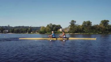 Kürek takımı eğitimi. İki beyaz erkek kürekçinin yan görüntüsü, bir kürek antrenmanı sırasında, Dnipro nehrinde bir sandalda oturan sporcu, sonbaharda sakin suda kürek çekiyor. 4K görüntü. Ukrayna, Kyiv 'deki şehir alanı.
