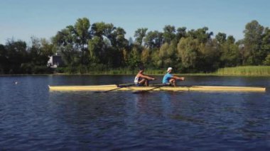 Kürek takımı eğitimi. İki beyaz erkek kürekçinin yan görüntüsü, bir kürek antrenmanı sırasında, Dnipro nehrinde bir sandalda oturan sporcu, sonbaharda sakin suda kürek çekiyor. 4K görüntü. Ukrayna, Kyiv 'deki şehir alanı.