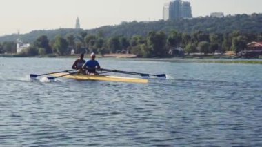 Kürek takımı eğitimi. İki beyaz erkek kürekçinin yan görüntüsü, bir kürek antrenmanı sırasında, Dnipro nehrinde bir sandalda oturan sporcu, sonbaharda sakin suda kürek çekiyor. 4K görüntü. Ukrayna, Kyiv 'deki şehir alanı.