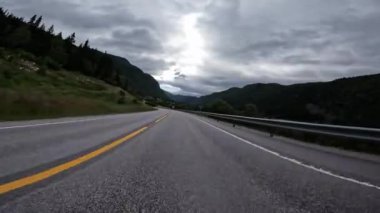 First person view of a nordic two-lane road, forest, mountains