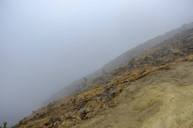 Bir dağ kraterinin portresi ve yanında kalın bir sis var. 