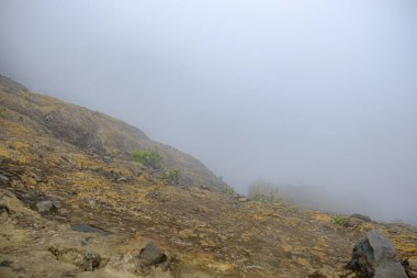 Bir dağ kraterinin portresi ve yanında kalın bir sis var. 