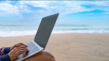 Bir kadın yaz mevsiminde plajda çalışmak için bilgisayar kullanıyor..
