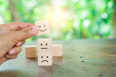 Müşteri memnuniyeti seviyesi ve memnuniyet anketi konsepti için tahtadan bir küp üzerinde gülen yüz simgesi.