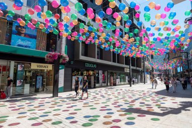 Andorra La Vella, Andorra: 15 Temmuz 2024: İnsanlar Meritxell adı verilen alışveriş caddesi boyunca yürüyorlar. Başkent Andorra la Vella, Andorra 'da 2024 yılında renkli toplarla süslenmişler..