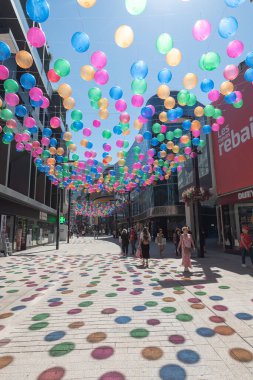 Andorra La Vella, Andorra: 15 Temmuz 2024: İnsanlar Meritxell adı verilen alışveriş caddesi boyunca yürüyorlar. Başkent Andorra la Vella, Andorra 'da 2024 yılında renkli toplarla süslenmişler..