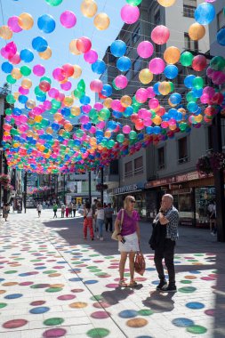 Andorra La Vella, Andorra: 15 Temmuz 2024: İnsanlar Meritxell adı verilen alışveriş caddesi boyunca yürüyorlar. Başkent Andorra la Vella, Andorra 'da 2024 yılında renkli toplarla süslenmişler..