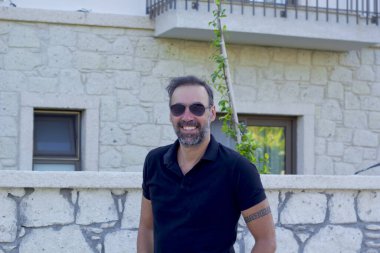 Kameraya gülümseyen güneş gözlüklü yakışıklı bir adam portresi.