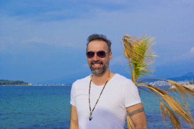 Yazın kumsalda kameraya gülümseyen yakışıklı bir adamın portresi.