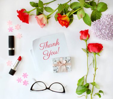 Kadın aksesuarları, kozmetik ürünleri, gül çiçekleri, bardaklar ve beyaz arka planda hediyeler çerçevesinde el yazısı alıntılar için teşekkürler. Üst görünüm, düz yatış modeli.