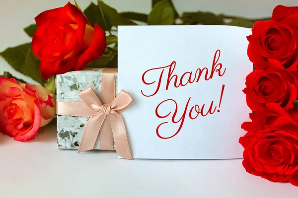 White card with Thank You inscription and flower buds of red roses on a white background: the concept of manifestation of gratitude and appreciation.