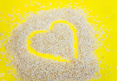 Sarı arka planda susam tohumundan yapılmış bir kalp. Sarı arkaplanda susam tohumları yakın plan.