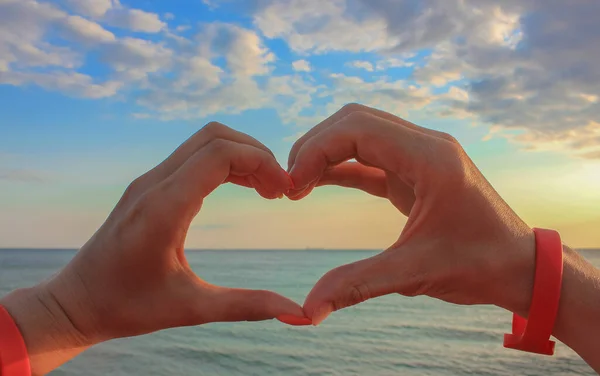 stock image The hands of woman and man in the form of hearts over blue skies, clouds and sea. Hands in the form of love hearts - love concept.