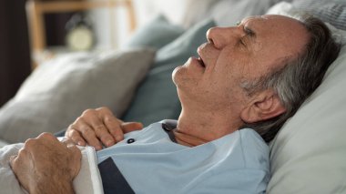 Yaşlı adam yatakta ağzı açık uyuyor.