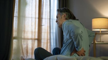 Sırtı ağrıyan yaşlı adam yatakta oturuyor.