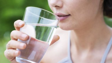 Woman holding a glass of water on green nature background clipart