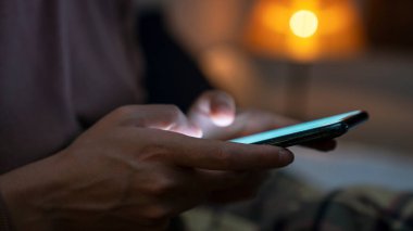 Geceleri yatakta uzanırken cep telefonu kullanan bir kadın.