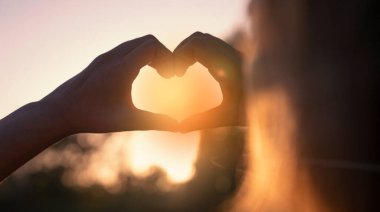 Gün batımında ellerle kalp şekillendiren kadın