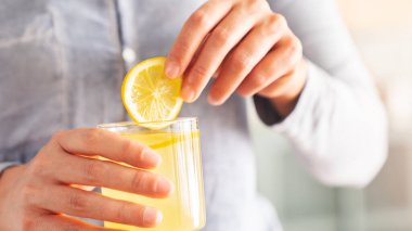 Bir bardak su, elinde limon dilimi olan kadın.